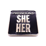 Picture shows frontside of pronouns badge - "Pronouns / She/ Her" silver metal and black enamel