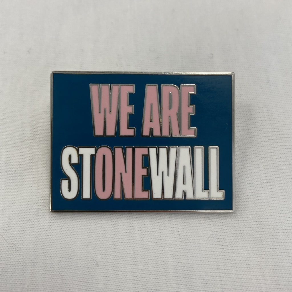 A square-ish pin badge with the words "We Are Stonewall" in capital letters. These are coloured a mixture of white and pink, where the pink words read: "We Are One." The background is teal.